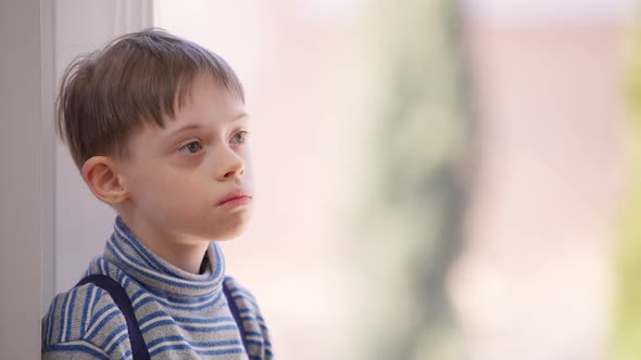 Caucasian Autistic Boy Standing at Window Indoors Looking Away alt