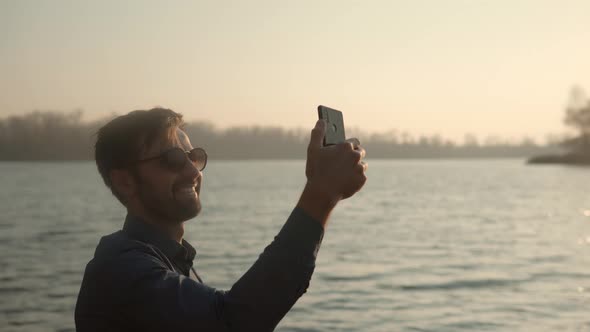 Man Hands Holding Mobile Phone And Taking Picture At Sunset. Guy Taking Photo of Sunset With Mobile. alt