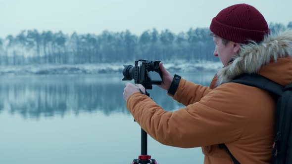 A Male Photographer Adjusts His Camera on a Tripod to Shoot the Edge of a Mountain Forest in the alt