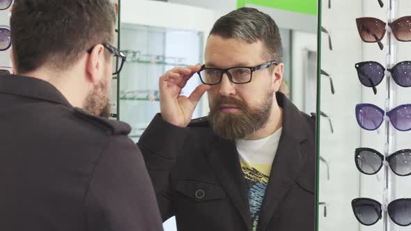 Mature Man Trying on New Glasses in Front If the Mirror at the Store alt