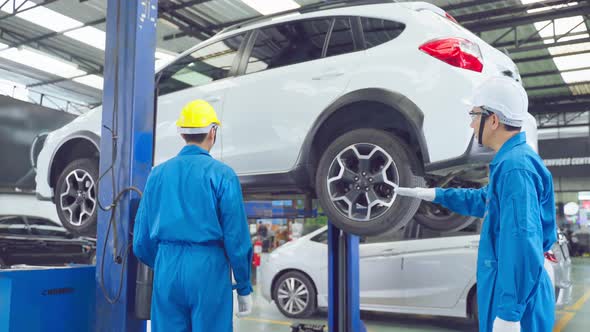 Asian automotive mechanic repairman look under car condition in garage. alt