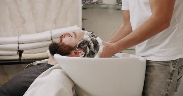 The Man in the Beauty Salon is Served Washing His Head with Shampoo and Water alt