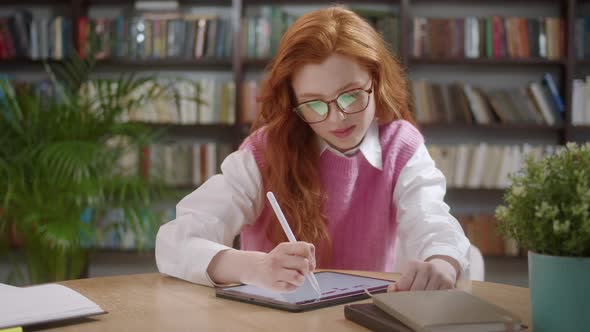 Attractive Student Woman with Red Hair Sketchig with Stylus on Digital Tablet Pc in Libraly