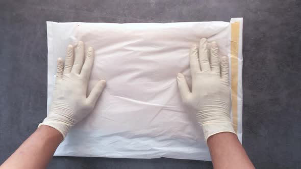 Hand in Latex Gloves Holding White Paper Bubble Envelope for Postal Ship alt
