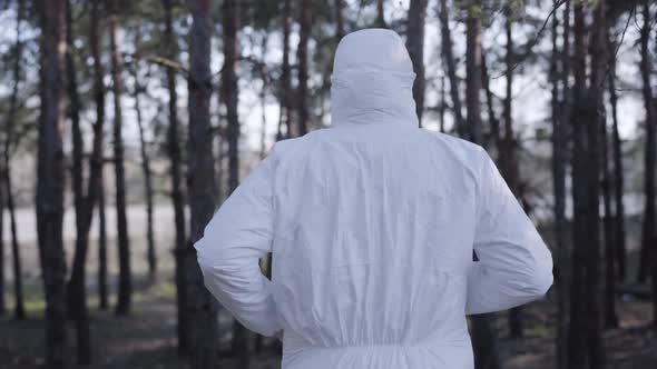 Back View of Young Caucasian Man in White Safety Suit, Protective Eyeglasses and Face Mask Running alt