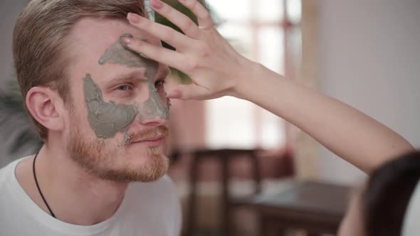 Family Skincare Routine at Home. Woman Applies Clay Beauty Mask on Man. Girlfriend Makes Cosmetology