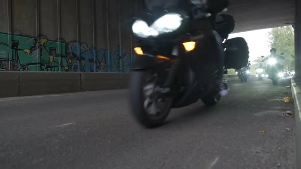 Large Group of Motorcyclists Driving Under a Bridge with Working Headlights