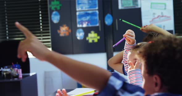 Schoolkid raising their hands in classroom alt
