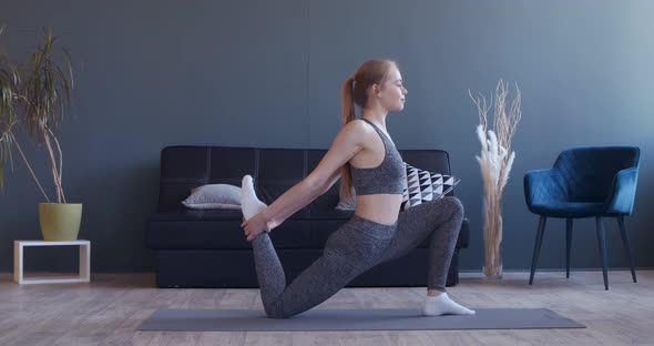 Young Woman Stretching Her Legs, Practicing Pilates at Home alt