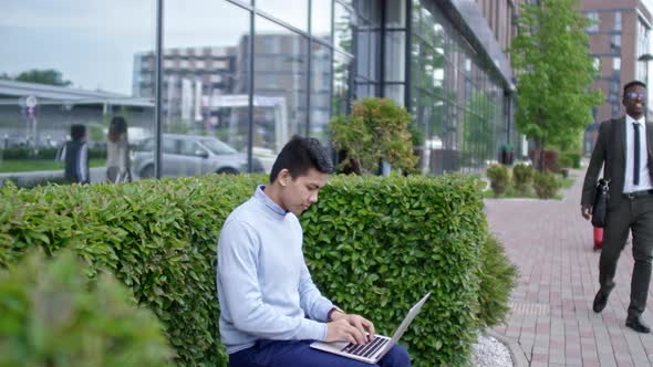 Young Asian Man Working on Laptop Outdoors in Downtown alt