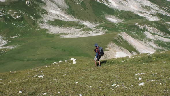 A man in the mountains with a backpack on his back goes down a grassy slope alt