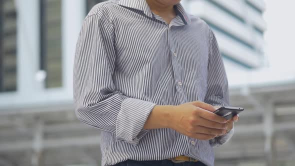 Portrait Asian businessman standing texting with a friend on smartphone at urban city background.