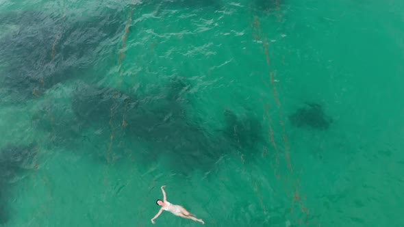 The Drone Flies Away From an Asian Girl in a White Bikini Floating in Green Transparent Ocean Water alt