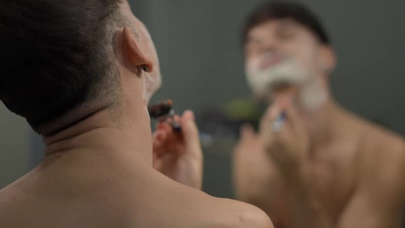 Back View Young Man Shaving Chin with Blurred Reflection in Mirror at Background alt