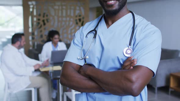 Portrait of african american male doctor smiling, with colleagues in discussion in background alt