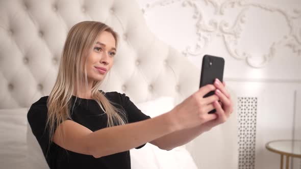 Woman Sits in Bed in Bedroom and Poses for Social Media App Videos Photos alt