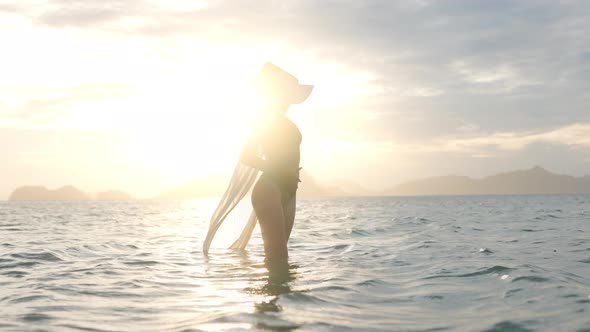 Woman In Bikini With Sun Hat Standing In Sea At Sunset alt