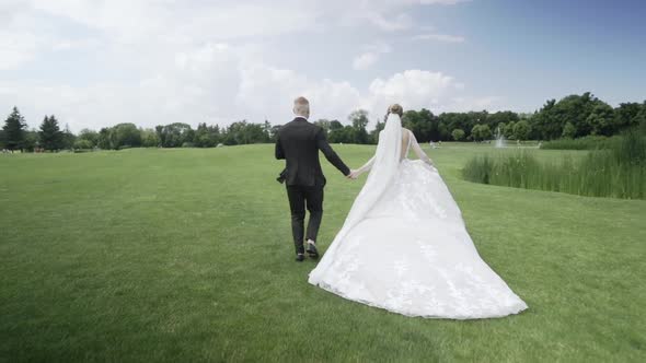 Newlyweds Running Together on the Green Field Rear View