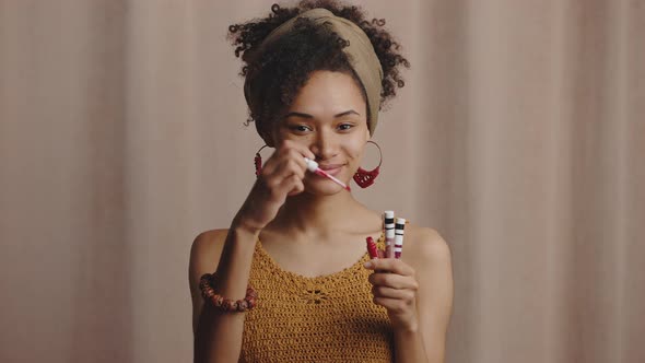 Young Stylish African American Lady Demonstrating Red Lipgloss Choosing Best Makeup Cosmetics Beige alt