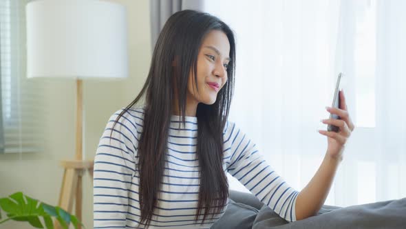 Asian beautiful woman sit on sofa and chat on mobile phone in house. alt