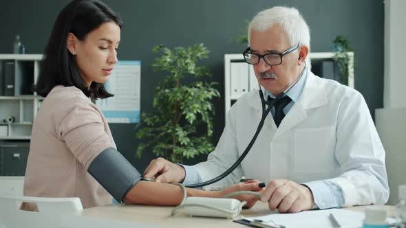 Doctor Checking Blood Pressure and Pulse Examining Female Patient in Hospital alt