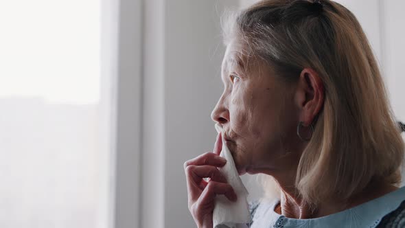 Elderly Woman Wiping Her Mouth with Napkin While Looking Through the Window alt