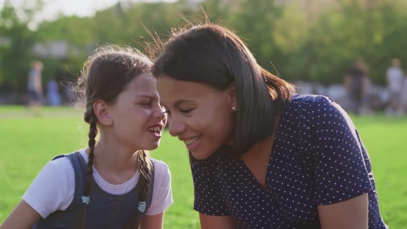 Closeup of Preteen Girl Whispering Secret to Surprised Mother at Park alt