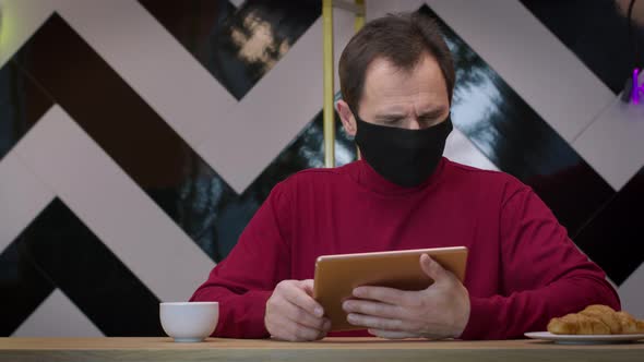 Handsome Man in Black Protective Mask Messaging and Chatting with Tablet in Cafe