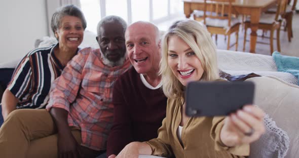 Two diverse senior couples sitting on a couch using a smartphone and taking a selfie alt