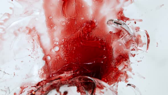 Super Slow Motion Top Shot of Breaking Glass with Red Wine on White Cloth at 1000Fps. alt