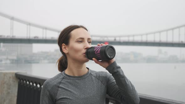 Thirsty Female runner drinking water from bottle after outdoor workouts. Running concept alt