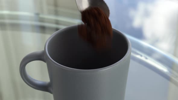 Two spoons of coffee to preparing a morning drink into grey mug, close-up view. alt