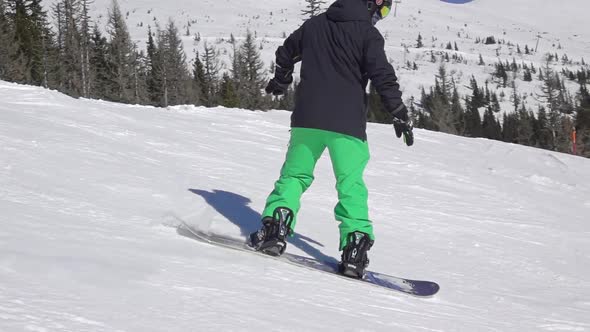 Snowboarder in a Green-Black Suit on a Ski Slope