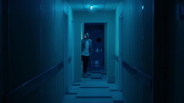 Man in a Coat Walks Along the Dark Blue Corridor of the Hospital