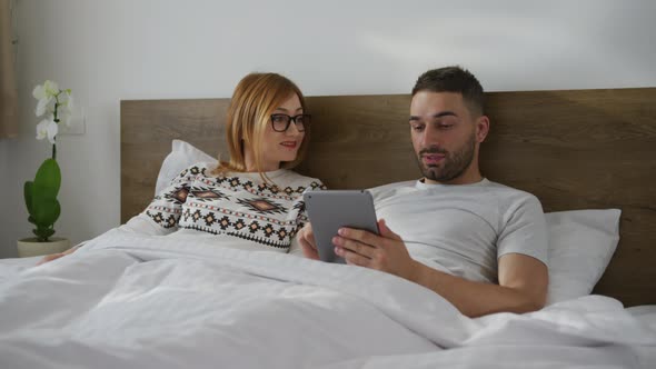 Couple lying in bed and searching on a tablet alt