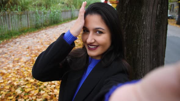 Young woman, in black and purple clothing, takes a selfie in an outdoor autum