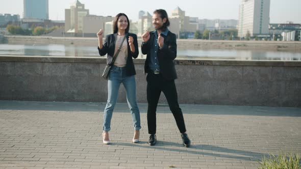 Mixed Race Man and Woman Dancing Outdoors Smiling Fooling Around Against Urban Background alt