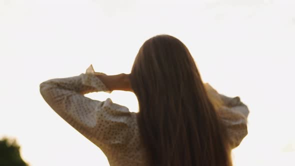 A Woman Seen From the Back Spreads Her Long Hair with Her Hands at Sunset alt