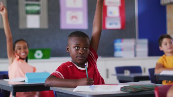 Diverse schoolchildren sitting in classroom raising hands to answer questions during lesson alt
