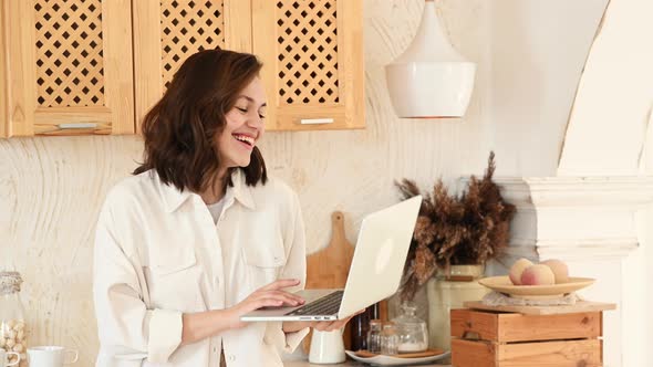 a Young Attractive Woman in a Bright Modern Kitchen Uses a Laptop for Video Communication alt