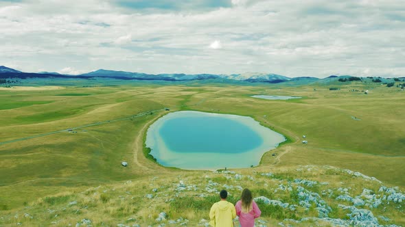 Couple Tourists Men and Women Stand on the Shore of a Picturesque Azure Lake a Summer Day alt