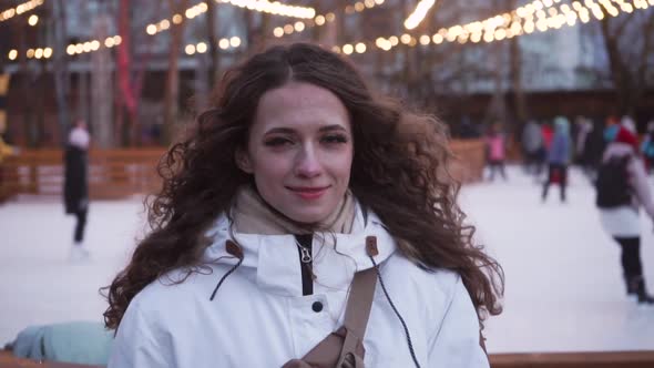 Curly Girl on the Background of the Ice Rink. Cheerful Young Woman with New Year's Sparkling Lights
