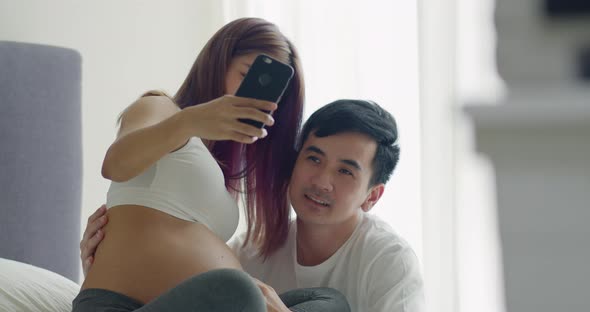 Happy caucasian husband with a pregnant wife taking selfie photos of her newborn baby.