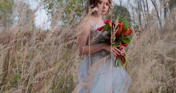 A Young Woman Dressed in a Gray Wedding Dress. She Has Flowers in Her Hand and Is in the Park alt
