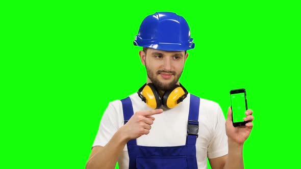 Man in a Builder's Suit Advertises a Smartphone. Green Screen. Mock Up alt