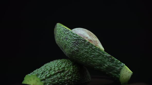 Two Halves of an Avocado Rotate in a Circle on a Black Background alt