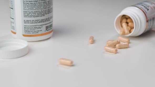 SLOW MOTION a Glass Jar Falls and Yellow Tablets Fall Out of It Onto a White Mate Table alt