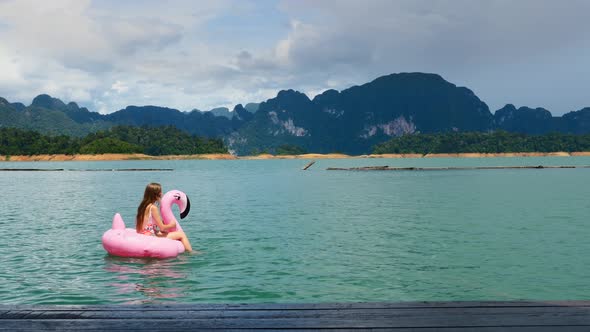 Happy Woman Have Fun and Fool Around at Pink Inflatable Flamingo on Blue Lake alt
