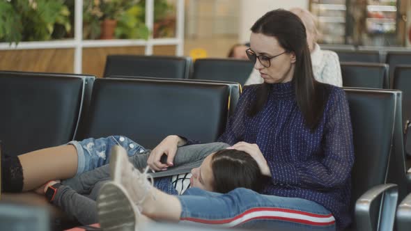 The Mother and Daughter in the Waiting Room of the Airport Sleeping on Chairs