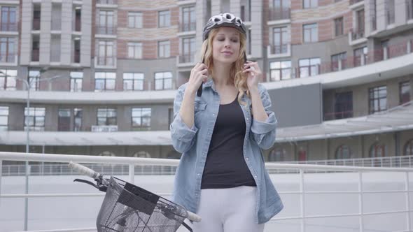 Pretty Blond Woman Putting a Bike Helmet on Her Head and Riding Her Bicycle Against the Background alt